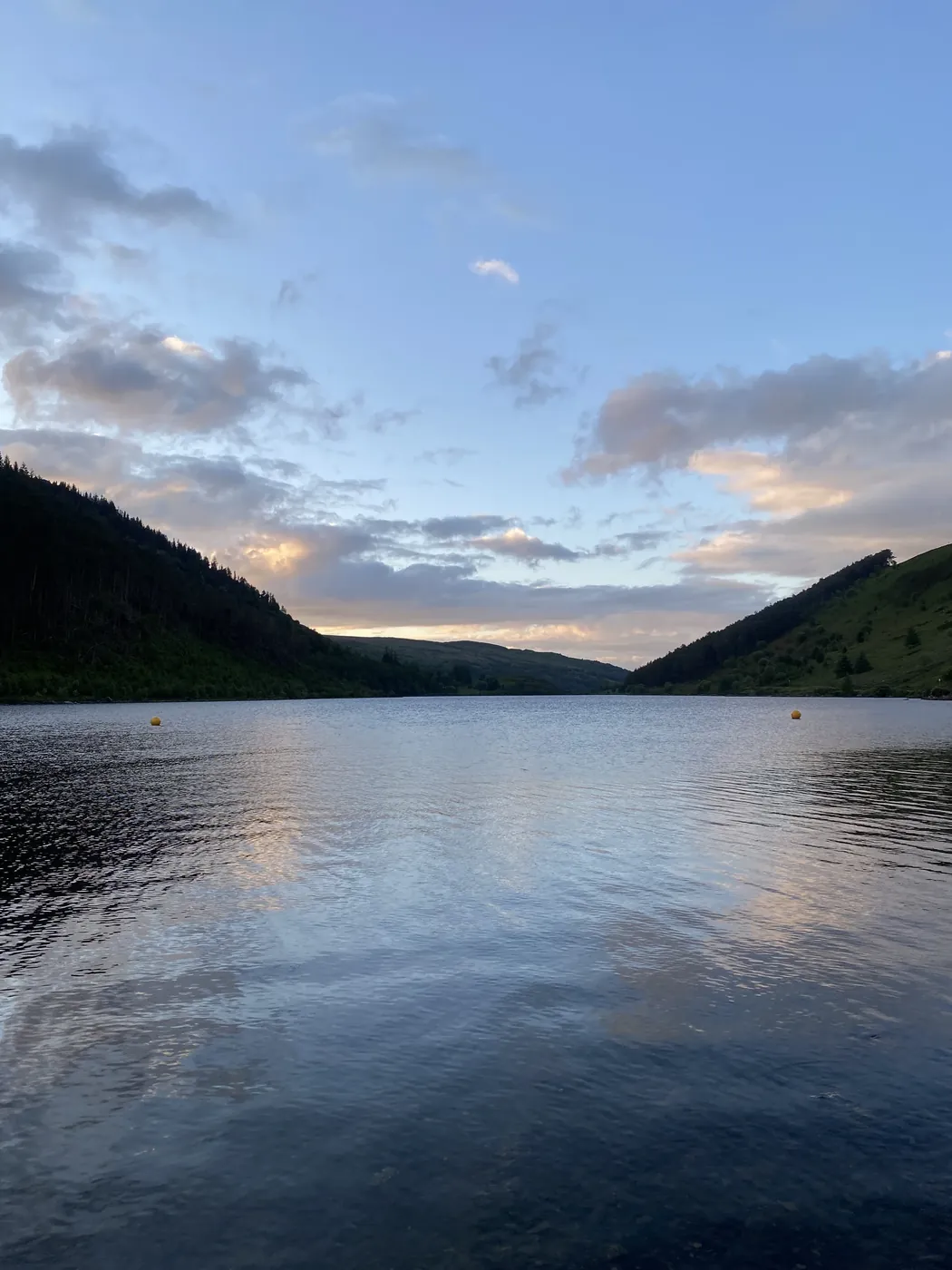 Still lake between wooded hills beneath an evening sky